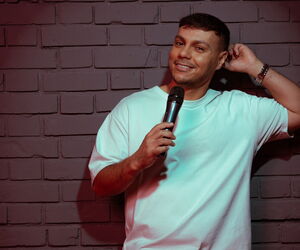 Osan Yaran vor einer Mauer stehend mit Mikrofon in die Kamera lachend.