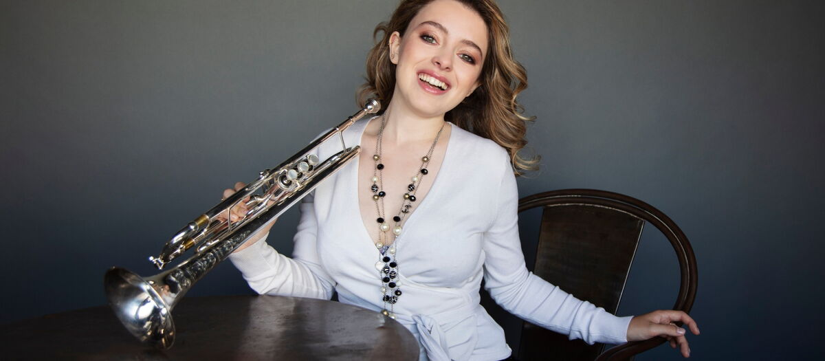 Luciene Renaudin Vari an einem Tisch sitzend und in die Kamera lachend.