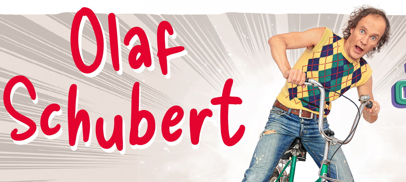 Olaf Schubert sitzt auf einem grünen Fahrrad mit einem überraschten Gesichtsausdruck.