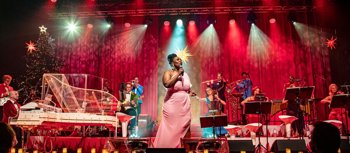 Max and Friends auf der Bühne und spielen Instrumente und singen. Die Bühne ist weihnachtlich geschmückt.