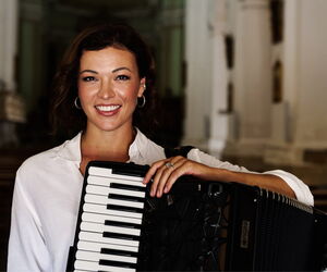 Ksenija Sidorova mit ihrem Akkordeon in die die Kamera lächelnd.