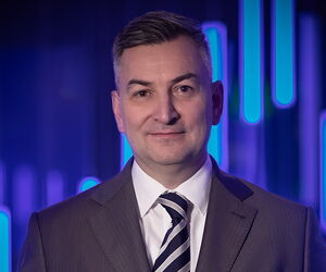 Portrait Markus Gürne in dunklem Anzug mit Krawatte vor blauem Hintergrund