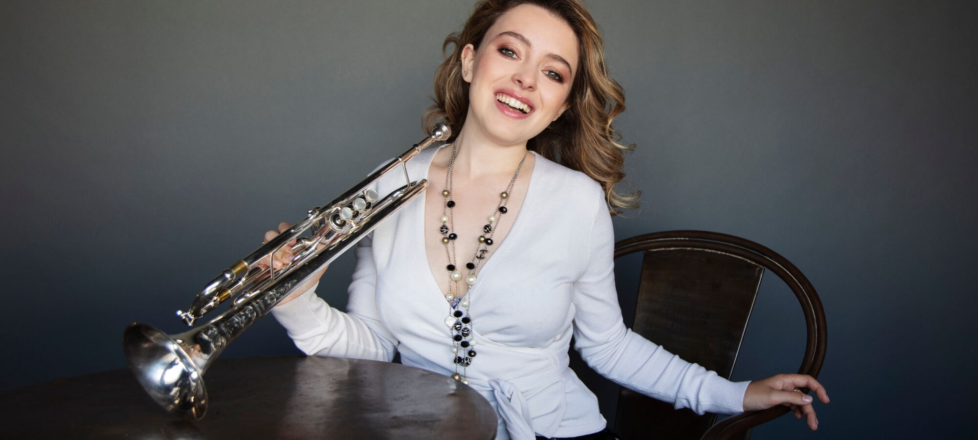 Luciene Renaudin Vari an einem Tisch sitzend und in die Kamera lachend.