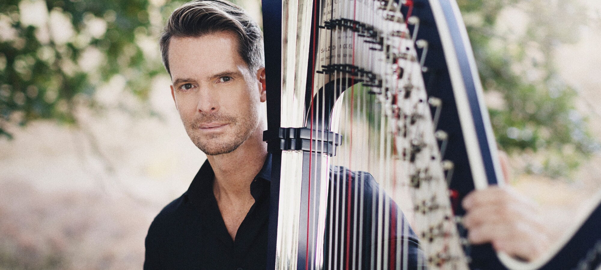 Nikolaj Lund vor einem Baum mit seiner Harfe.