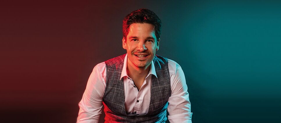 Alain Frei sitzend vor einem blau rotem Hintergrund