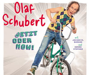 Olaf Schubert sitzt auf einem grünen Fahrrad mit einem überraschten Gesichtsausdruck.