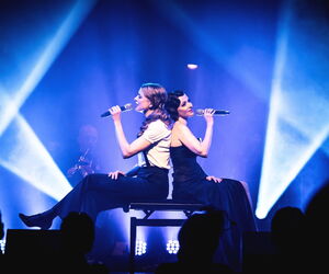 Die zwei Protagonisten Rücken an Rücken auf der Bühne sitzen und singend.