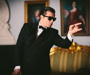 Darsteller Falco in schwarzem Anzug mit Fliege und Sonnenbrille von der Seite.