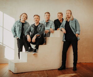 Bandmitglieder KARAT vor einer weißen Wand leger in schwarzer Kleidung und Jeansjacken.