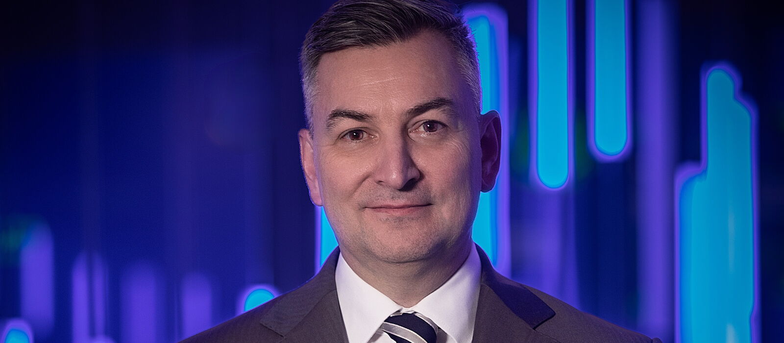 Portrait Markus Gürne in dunklem Anzug mit Krawatte vor blauem Hintergrund