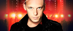 Billy Andrews in die Kamera schauend vor einem rot beleuchteten Bühnenhintergrund.