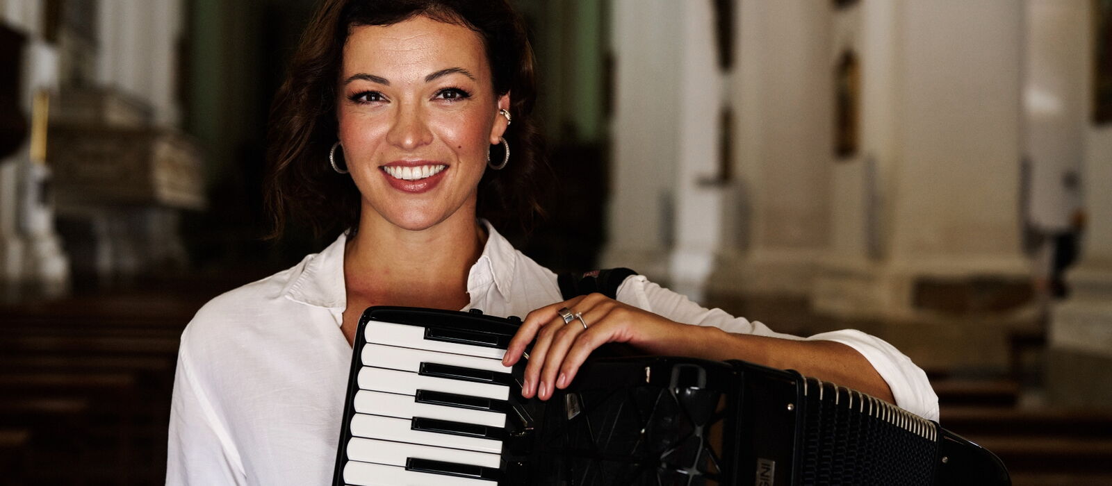 Ksenija Sidorova mit ihrem Akkordeon in die die Kamera lächelnd.