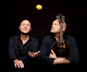 die feisten, einer mit Ukulele und der andere eine Zitrone hochwerfend vor schwarzem Hintergrund