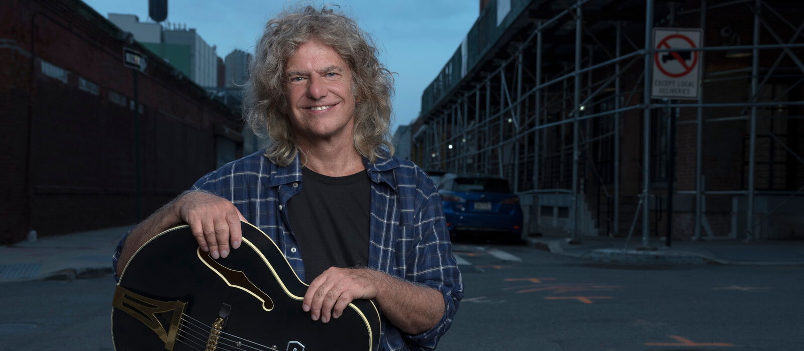 Pat Metheny mit Gitarre ins Bild lachend, im Hintergrund eine Straße
