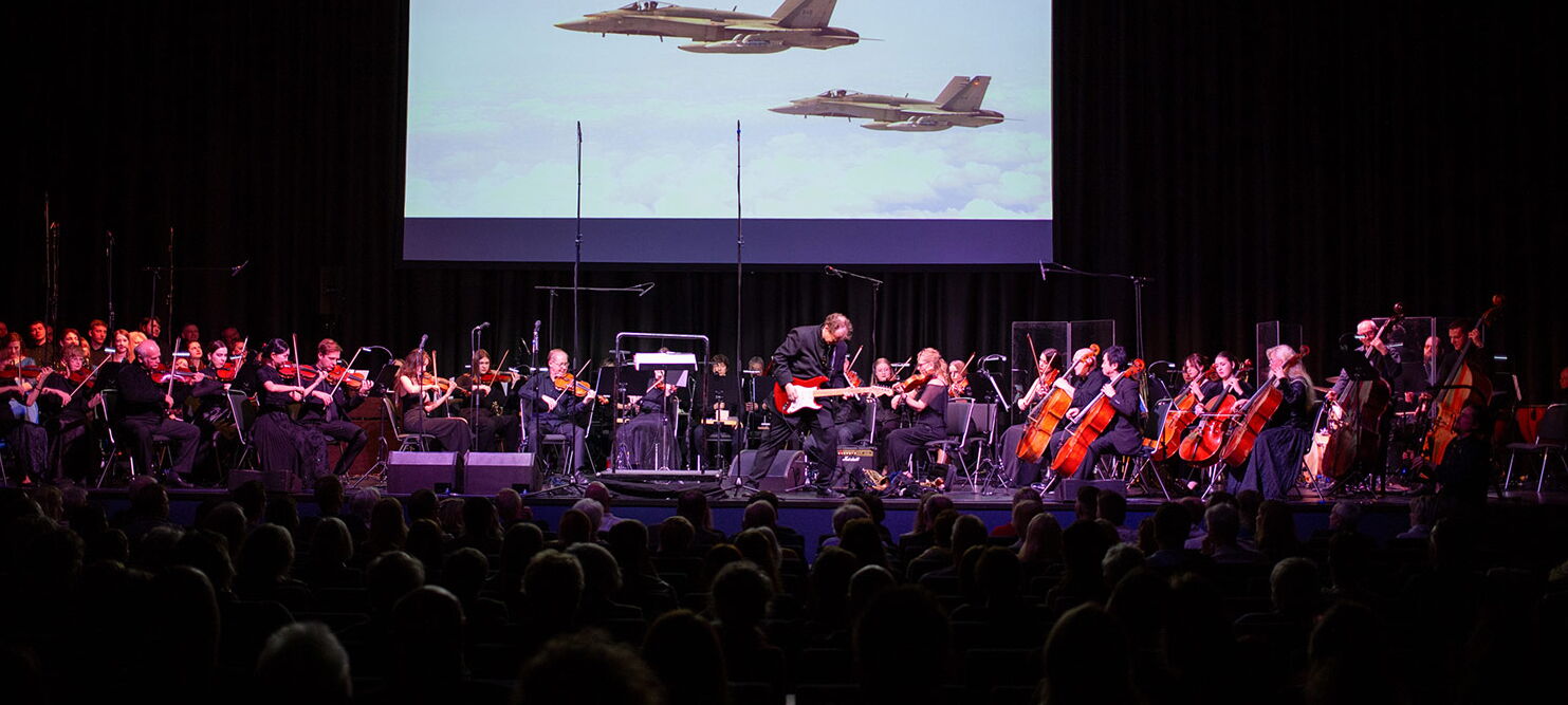 Das Orchester auf der Bühne, darüber eine Videowand mit zwei Düsenjets.
