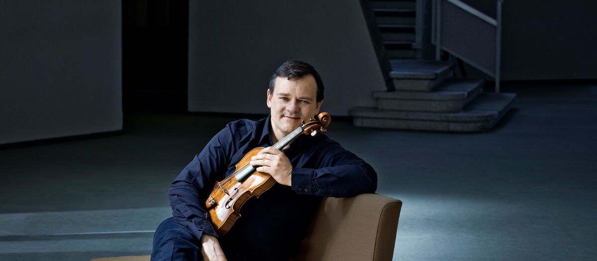 Frank Peter Zimmermann auf einem Sofa sitzend mit seiner Violine in der Hand.