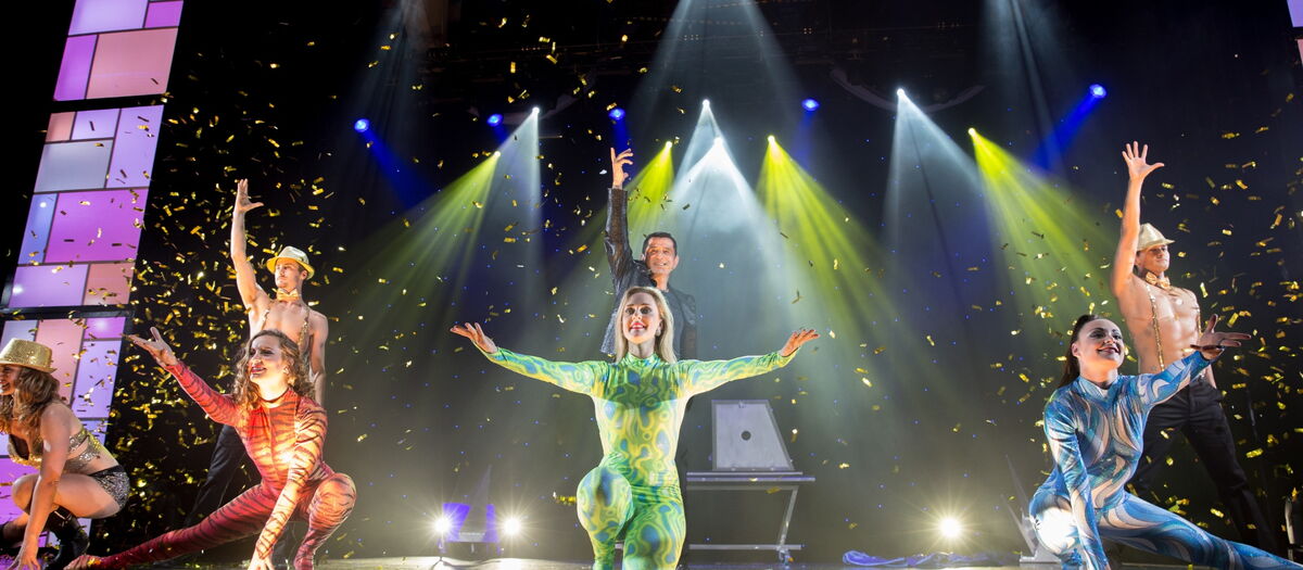 Magier mit 3 Tänzerinnen auf der Bühne mit buntem Licht