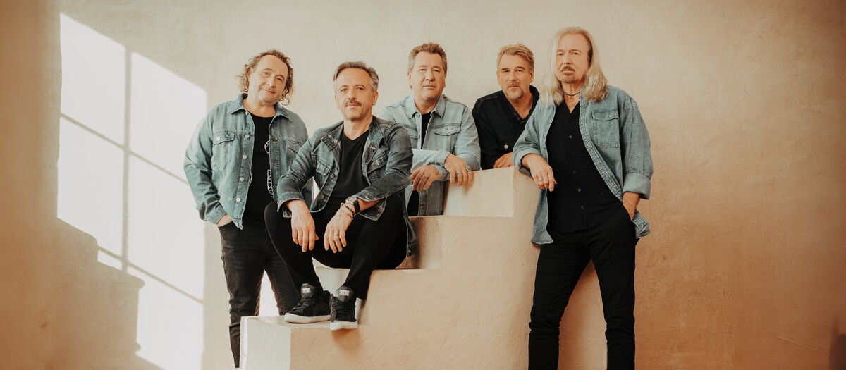 Bandmitglieder KARAT vor einer weißen Wand leger in schwarzer Kleidung und Jeansjacken.