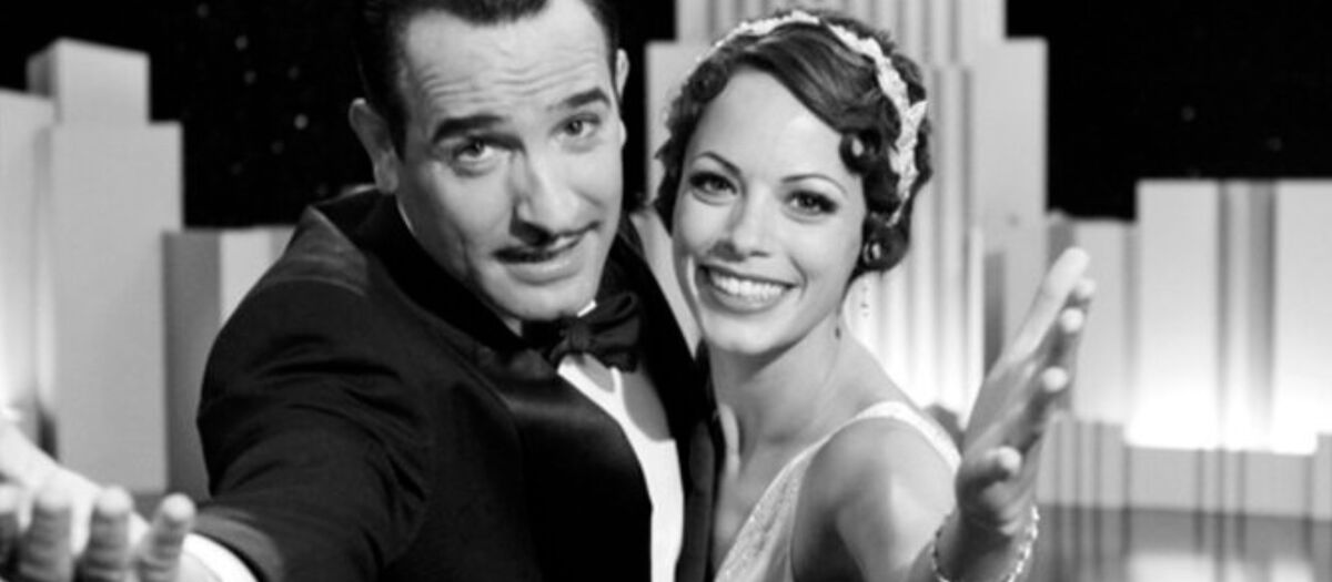 Zwei elegant gekleidete Personen aus dem 60er-Jahren tanzen gemeinsam in Art‑Deco‑Kulisse