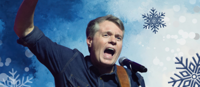 Jimmy Kelly vor einem winterlichen Hintergrund mit gezeichneten Eisblumen, mit einer Gitarre singend.