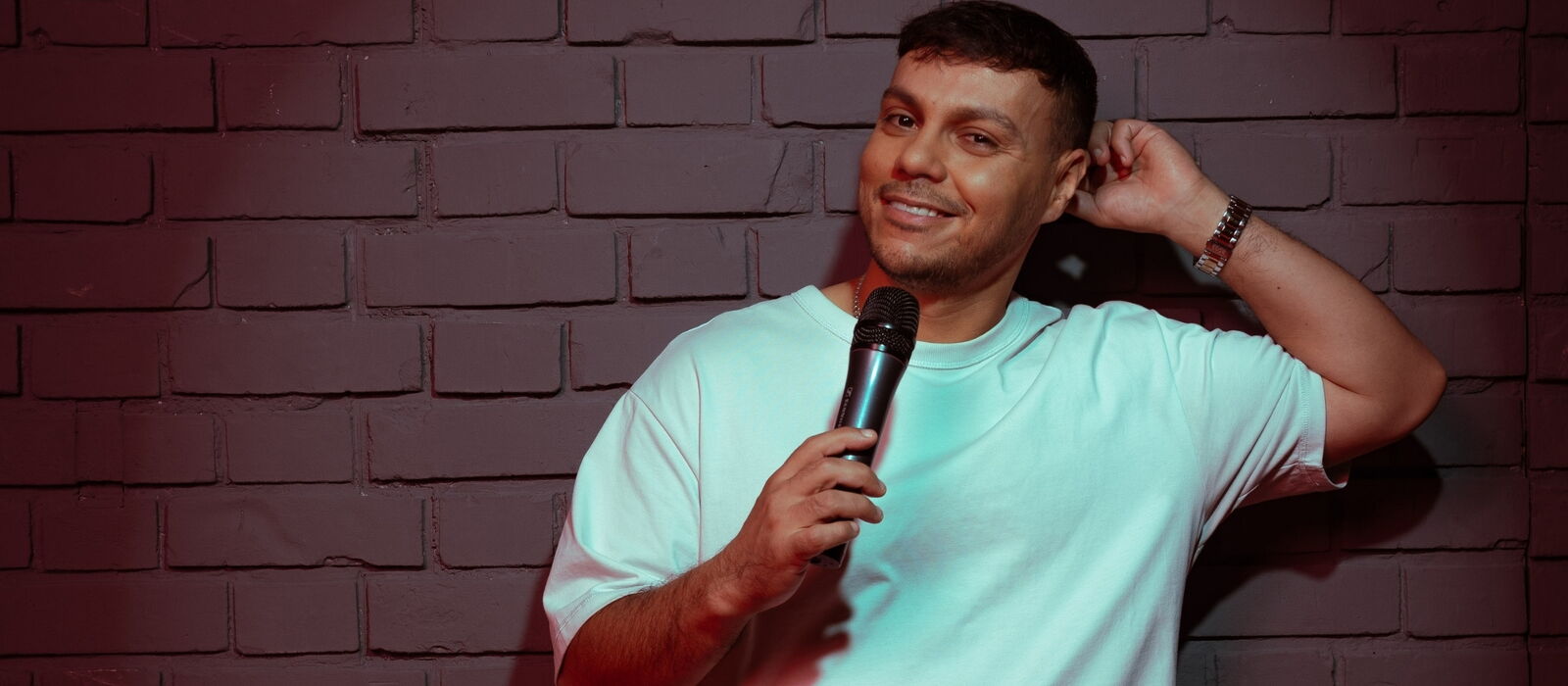 Osan Yaran vor einer Mauer stehend mit Mikrofon in die Kamera lachend.