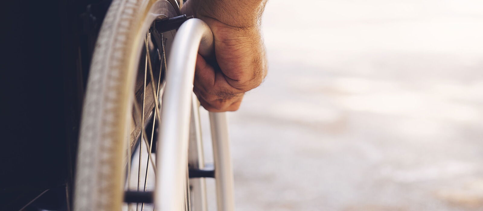 Mann im Rollstuhl, nur der Reifen und eine Hand erkennbar