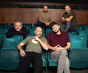 Die Bandmitglieder in einem Kino verteilt sitzend und in die Kamera schauend.