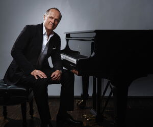 Joja Wendt sitzt in einem Schwarzen Anzug an einem Klavier