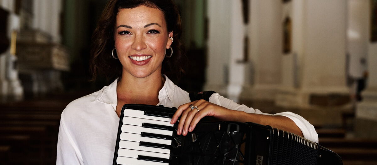 Ksenija Sidorova mit ihrem Akkordeon in die die Kamera lächelnd.