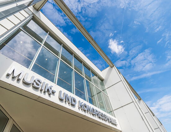 Außenansicht des Eingangs der Musik- und Kongresshalle Lübeck nach oben mit blauem Himmel