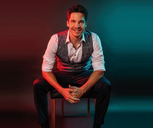 Alain Frei sitzend vor einem blau rotem Hintergrund