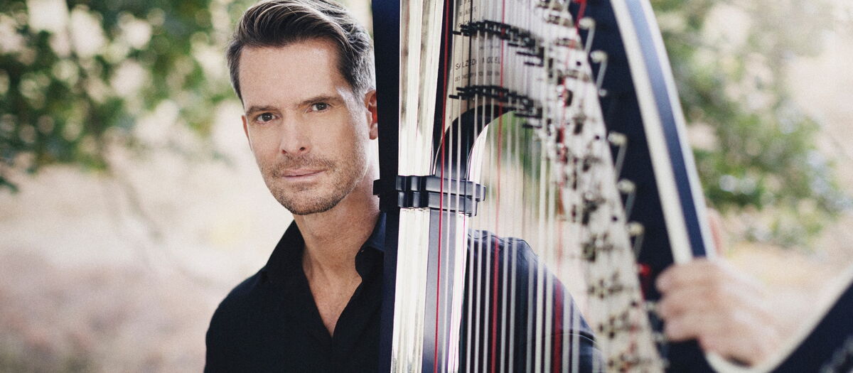 Nikolaj Lund vor einem Baum mit seiner Harfe.