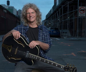 Pat Metheny mit Gitarre ins Bild lachend, im Hintergrund eine Straße