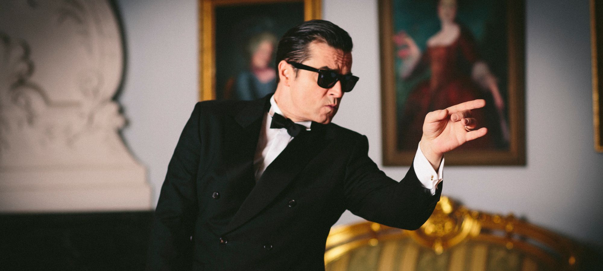 Darsteller Falco in schwarzem Anzug mit Fliege und Sonnenbrille von der Seite.