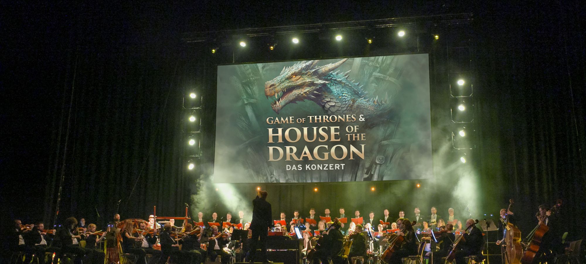 Orchester auf der Bühne mit Dirigent und das Artwork mit Schriftzug und Drachen oberhalb.